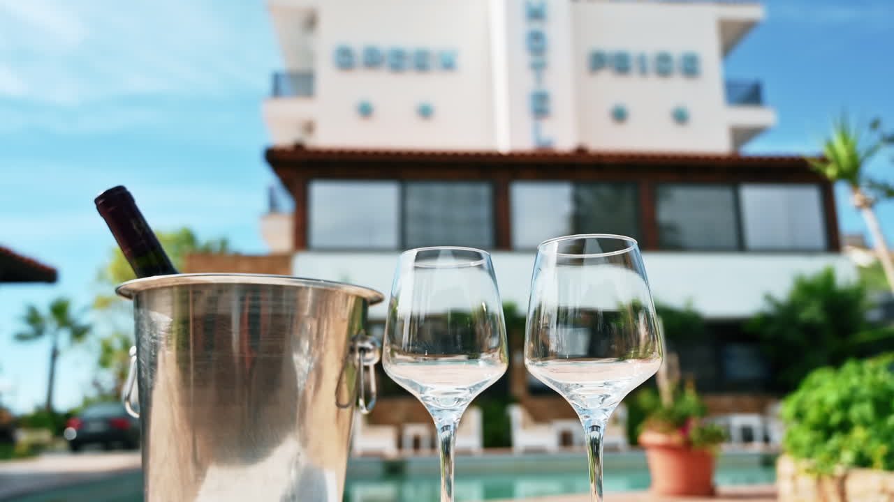 Bucket with ice and wine bottle, two wine glasses with pool and hotel on the background, Greece