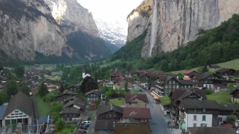 aerial of a village in a mountainous valley with a tall waterfall