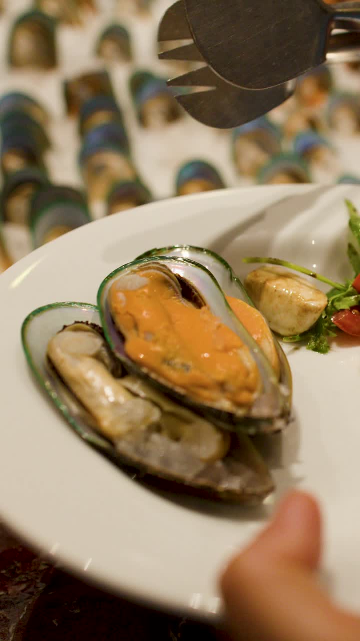 A person uses metal tongs to select fresh mussels from an ice-filled restaurant buffet display