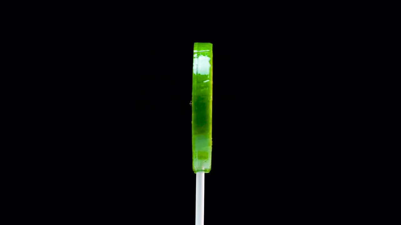 Rotating green fruit lollipop on a black background. Caramel lollipop. Sweets for children