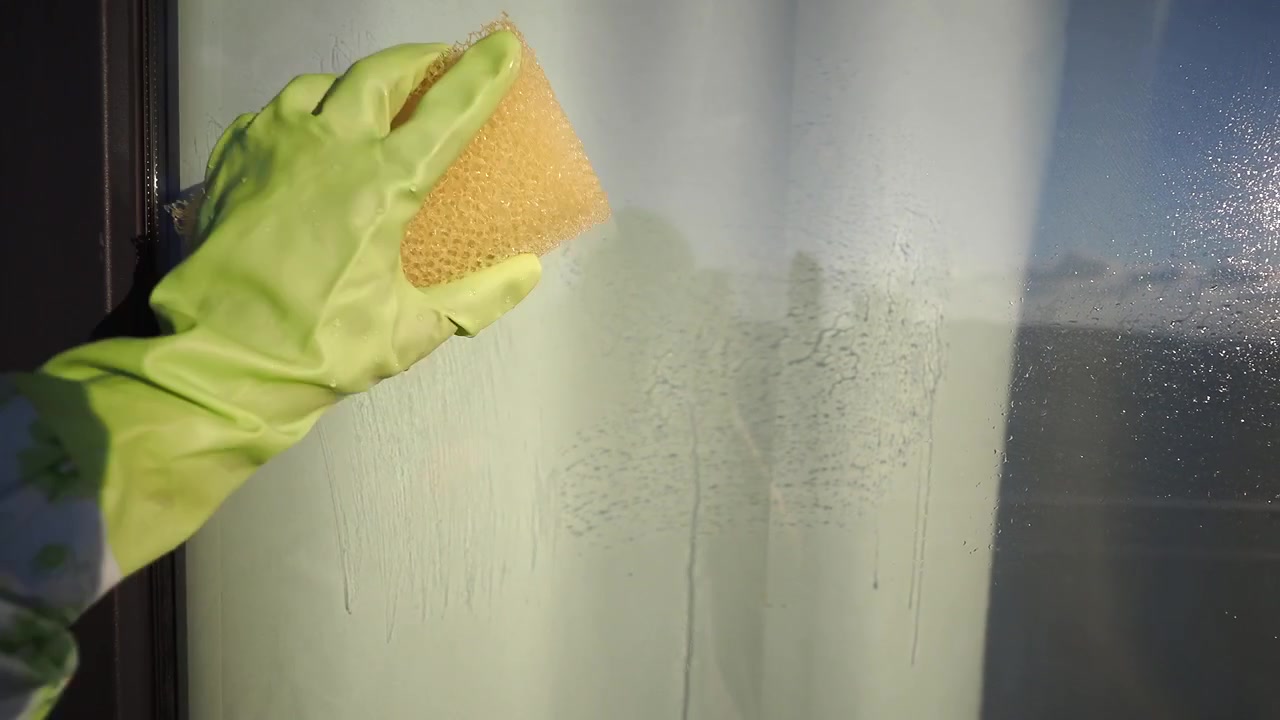 Person Wearing Green Rubber Glove Cleaning Window with Sponge