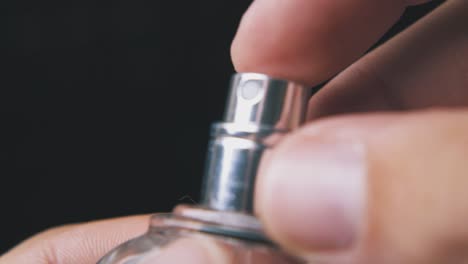 person sprays perfume from glass bottle on dark background