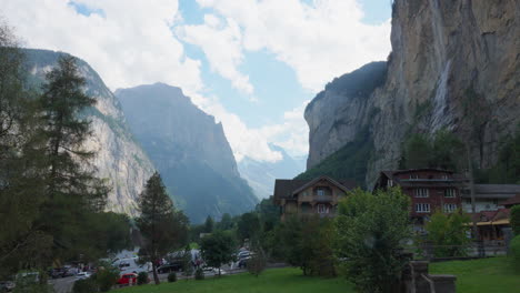 Tall-rocky-mountain-cliffs-tower-above-village-in-lowlands-of-valley,-europe