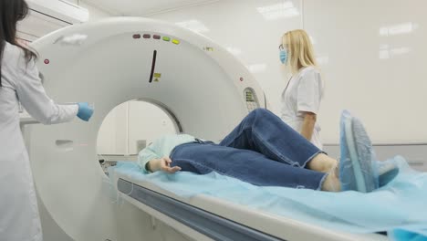 female patient is undergoing ct or mri scan under supervision of two qualified radiologists in modern medical clinic. patient lying on a ct or mri scan table, moving outside the machine