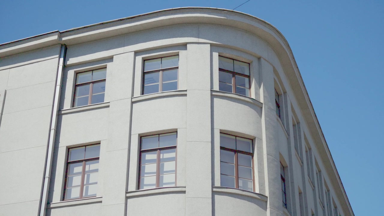 Plano de baixo ângulo destacando um elegante canto arquitetônico arredondado de um edifício de vários andares restaurado, sob um céu azul claro e brilhante na região de Daugavpils, Latgale.
