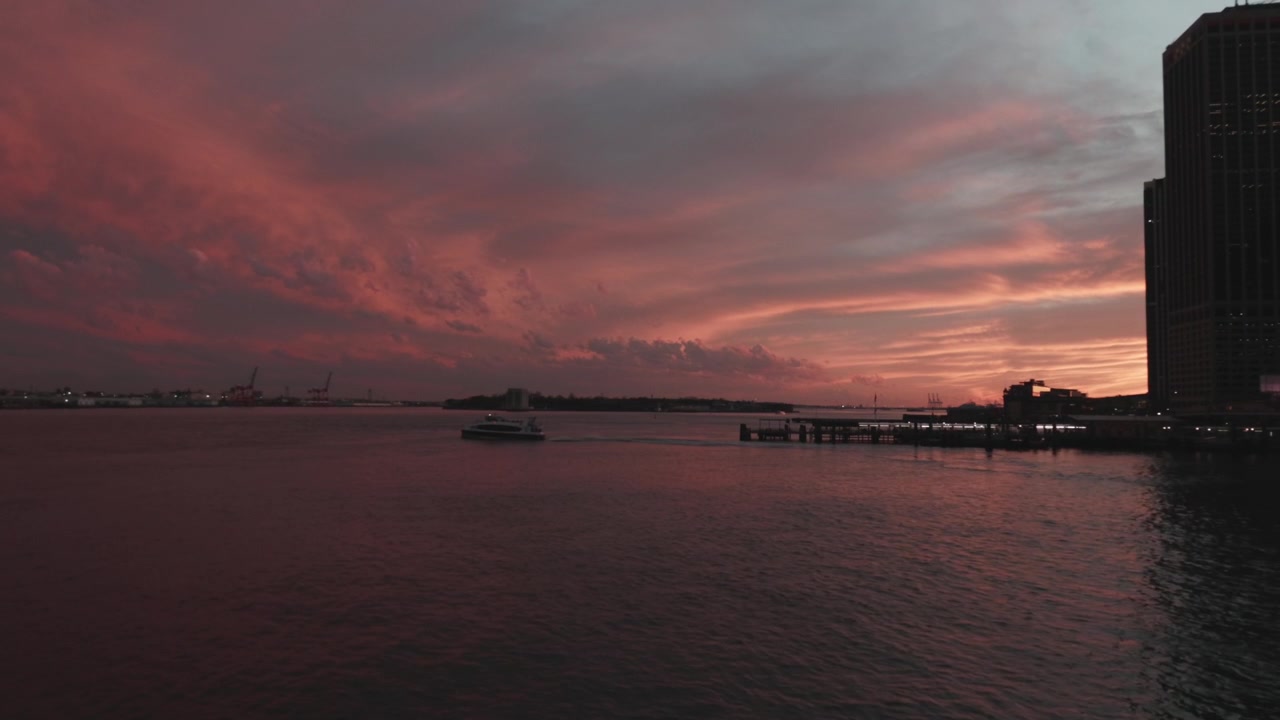 A boat glides across the waterfront as a dramatic red and orange sky creates a striking backdrop at dusk. Ideal for urban landscape features or atmospheric scene settings.