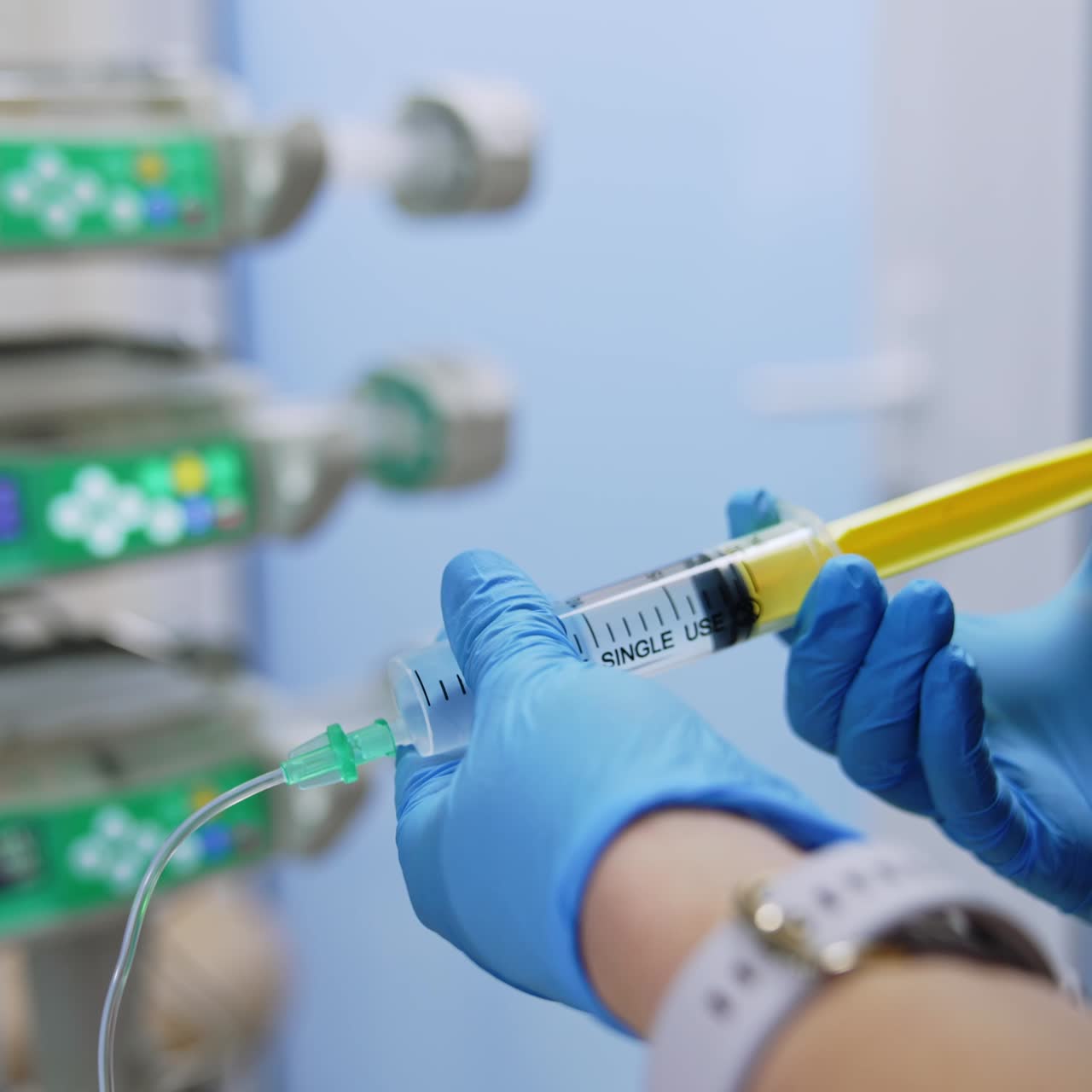 Gloved hands holding the syringe and pushing its forcer. Medic puts the syringe attached to a wire on infusion pump machine