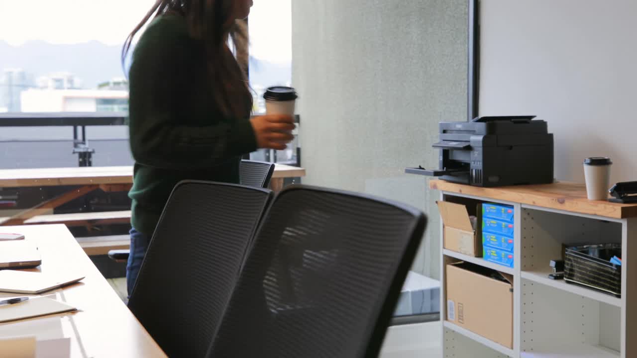 vista frontal de una joven empresaria asiática caminando con una taza de café en una oficina moderna 4k
