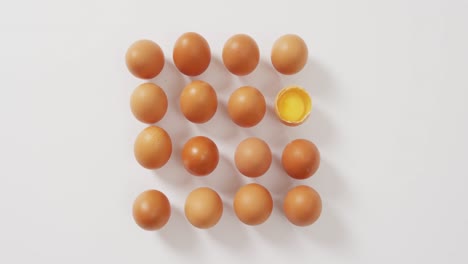 Close-up-of-half-broken-egg-with-among-other-eggs-on-white-surface