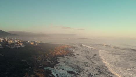 Aerial-cinematic-look-showing-a-rocky-shoreline-centre-frame-with-coastal-homes-on-the-left-looking-over-boulders-and-ocean-view-to-the-right-as-waves-and-tides-in-tranquil-town-vermont