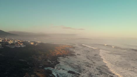 aerial cinematic look showing a rocky shoreline centre frame with coastal homes on the left looking over boulders and ocean view to the right as waves and tides in tranquil town vermont