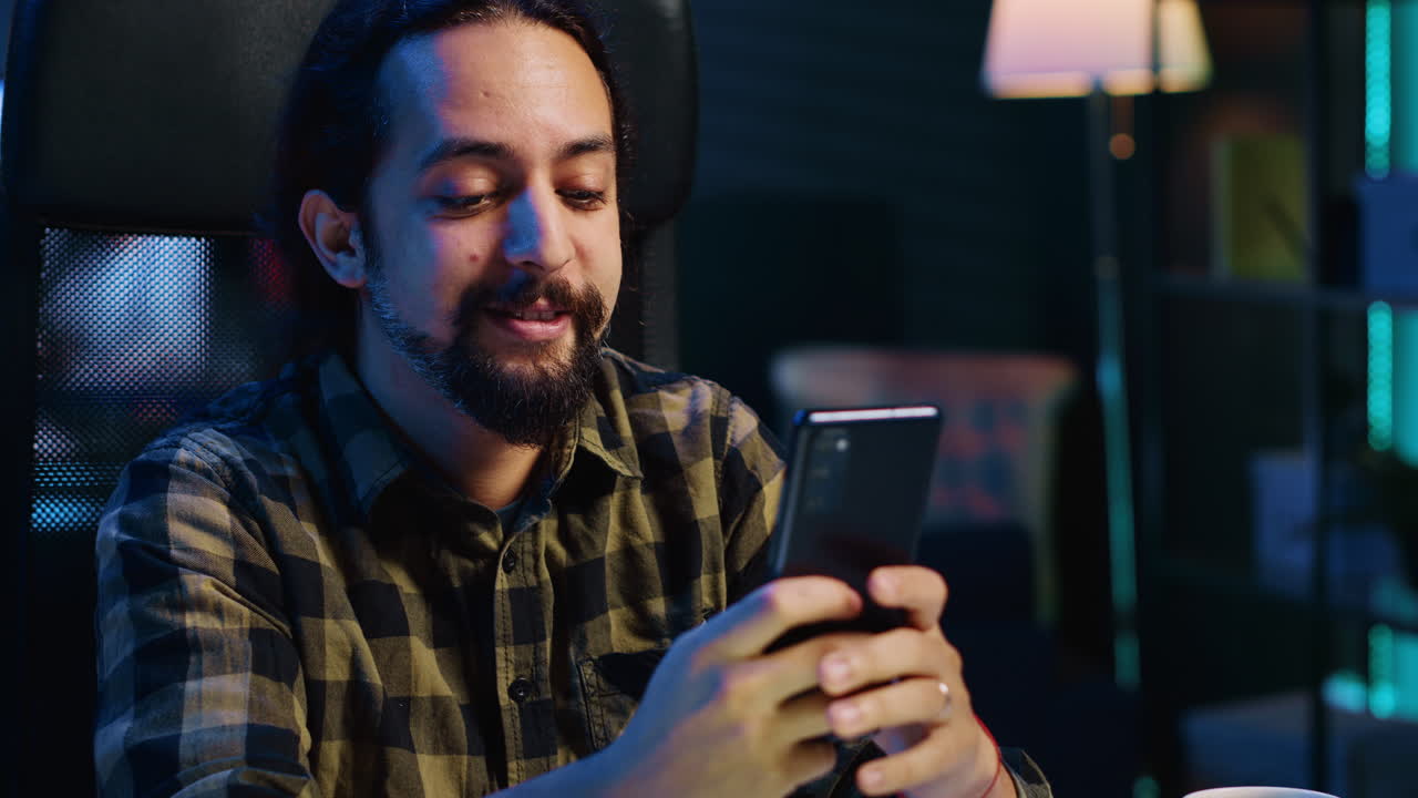 Uomo sorridente a casa che messaggia con il migliore amico sullo smartphone, in pausa dal lavoro.