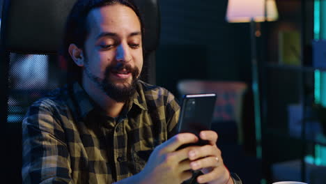 hombre sonriente en casa enviando mensajes de texto a su mejor amigo en su teléfono inteligente, tomando un descanso del trabajo