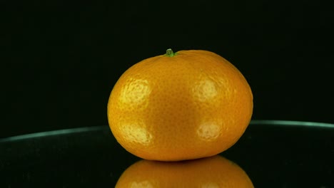 one lone orange rotates on mirrored base against black background