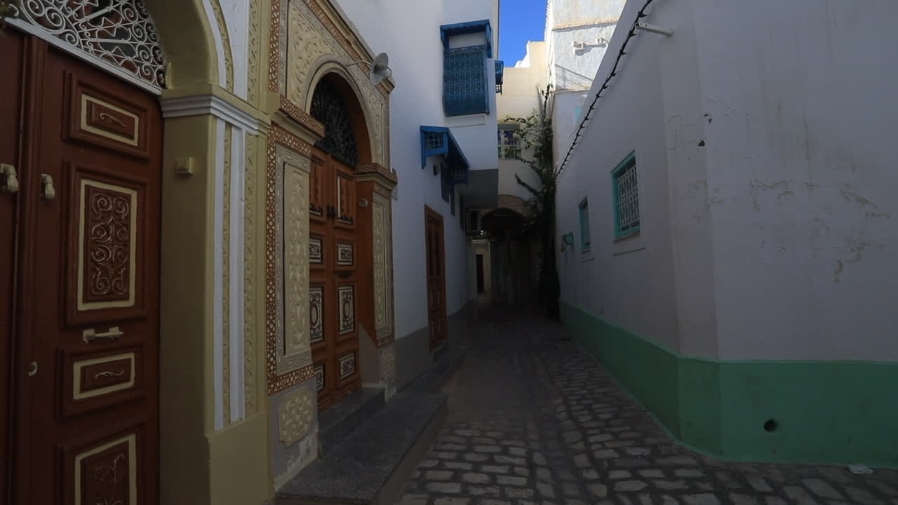 Narrow street in Tunisia lined with traditional buildings and colorful doors under clear sky