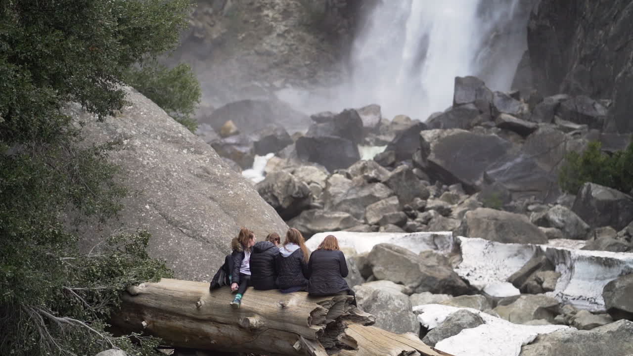 Slow motion shot of four college age girls sitting on a log looking at a waterfall in Yosemite National Park