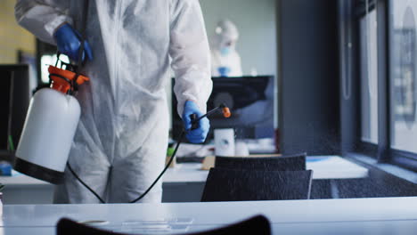 mid section of health worker wearing protective clothes cleaning the office using disinfectant spray