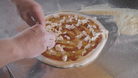 close up view of a chef spreading cheese on pizza dough on a restaurant kitchen countertop