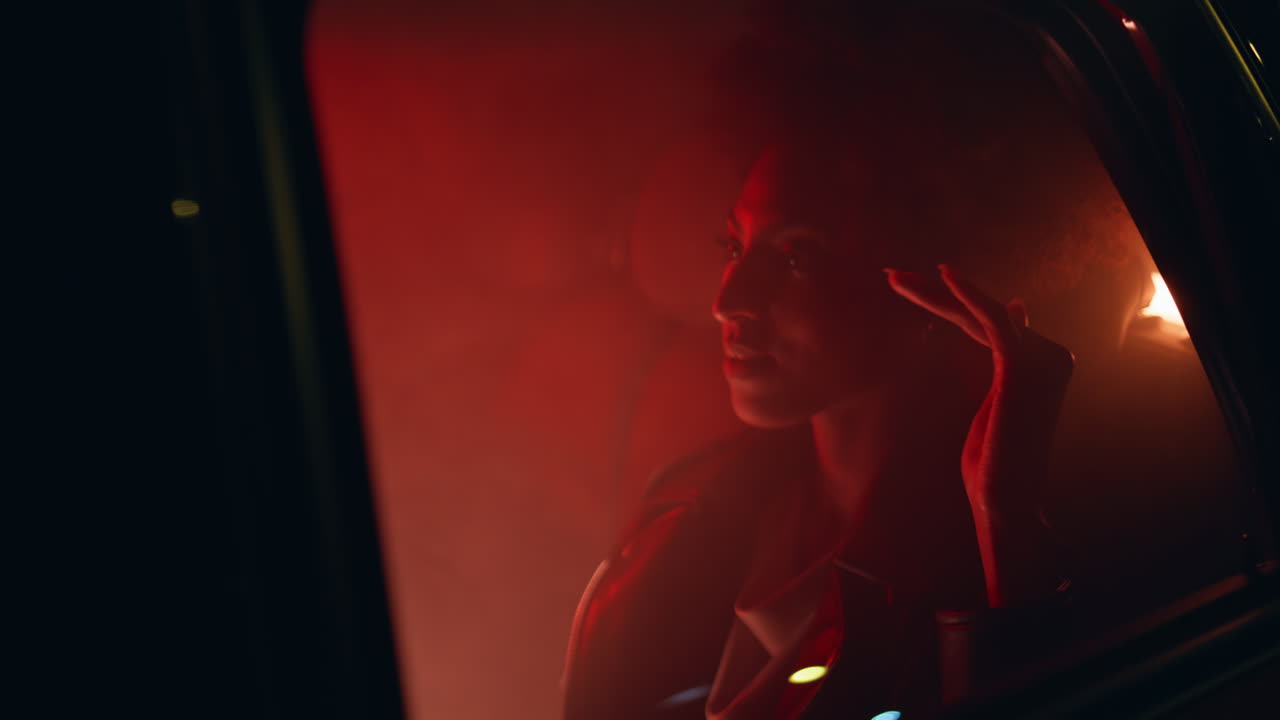 Donna che si rilassa con luci rosse al neon sul sedile posteriore dell'auto, vista ravvicinata attraverso il finestrino
