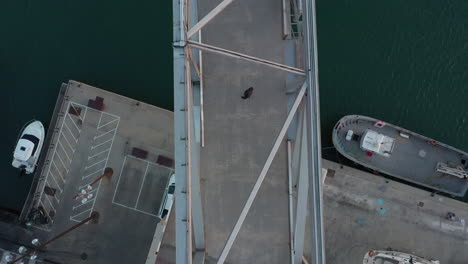 birdseye aerial view above male walking across bridge looking behind and begins to run scared