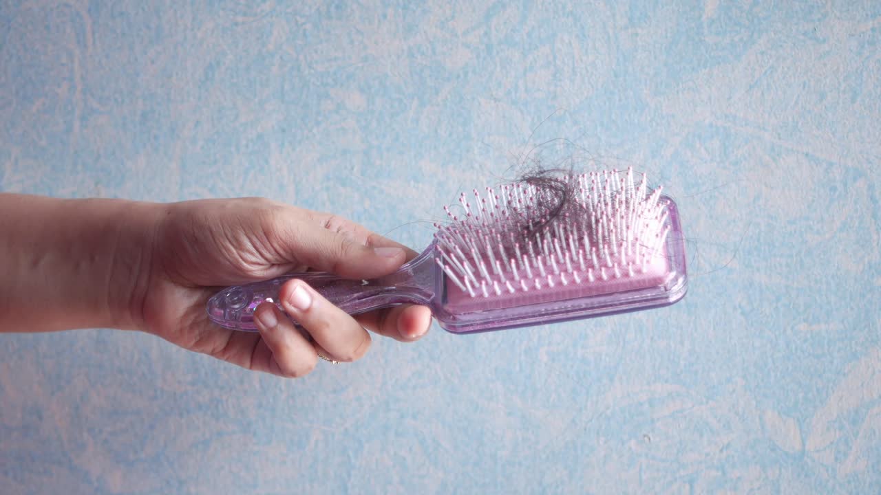 Woman's Hand Holding a Purple Comb with Lost Hair