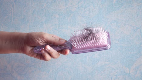 woman's hand holding a purple comb with lost hair