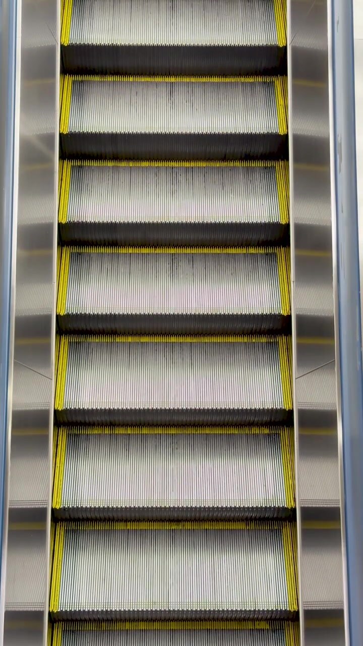Et statisk højvinkelbillede viser sølvfarvede metalrulletrappetrin, der bevæger sig opad i Tokyo.