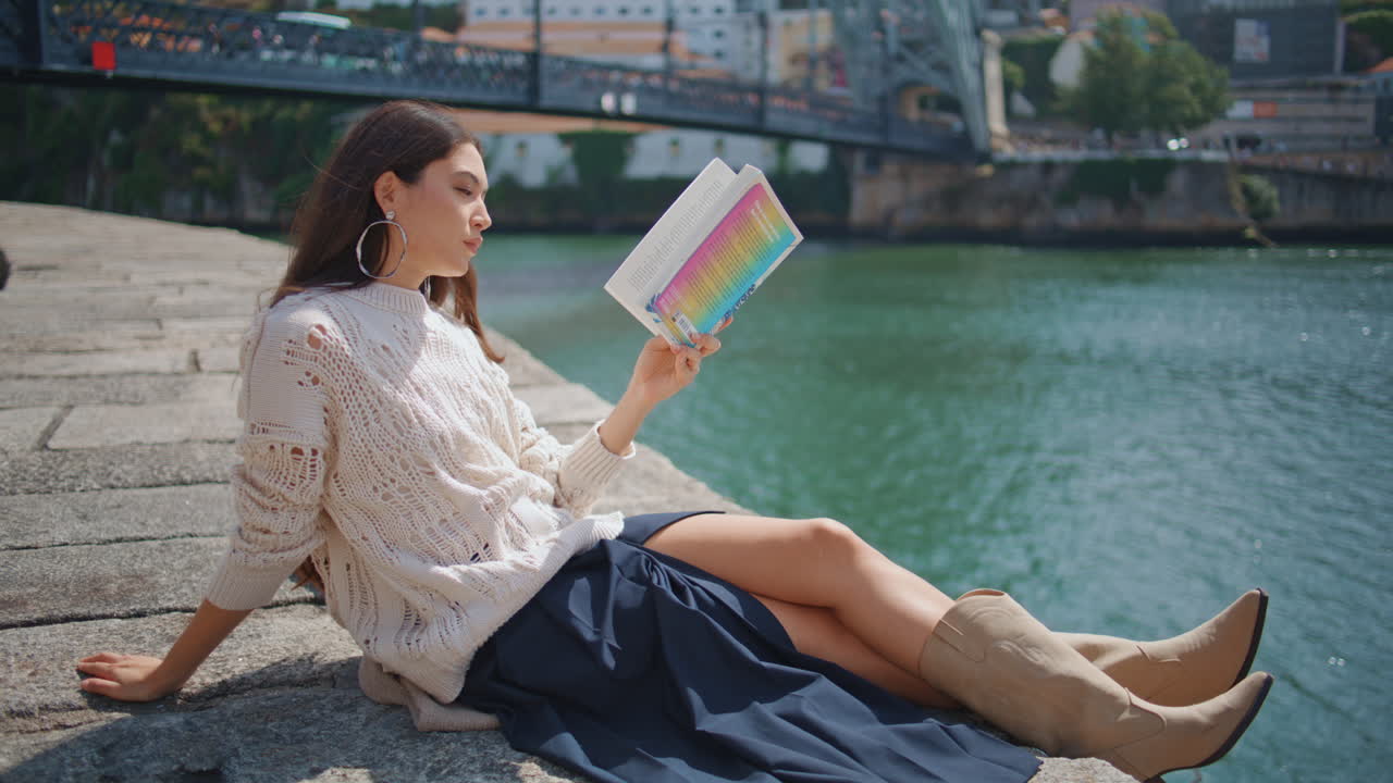 Young woman reading book sitting river embankment zoom on. Focused girl relaxing