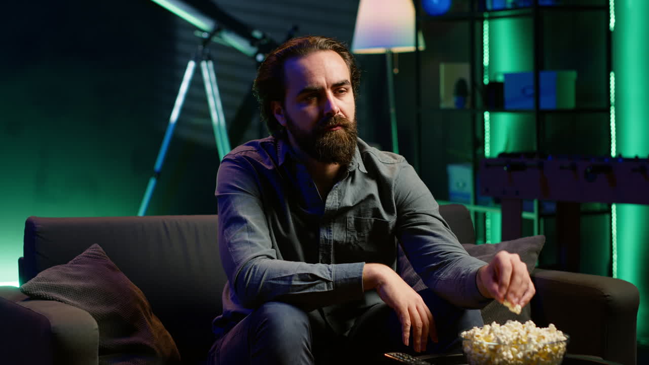 남자 는 tv 에서 케이블 프로그램 을 보는 동안 팝콘 의 그 을 즐기고 미소 짓고 있다