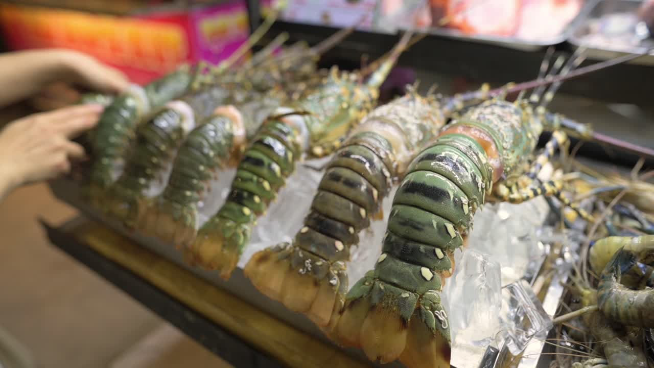 Fresh Lobsters On Ice, Vietnamese Market Hands Of Vendor Arranging Large Green Prawns On Ice Tray, Closeup Of Tails And Shells, Chilled Seafood Display At Busy Street Stall With Colorful