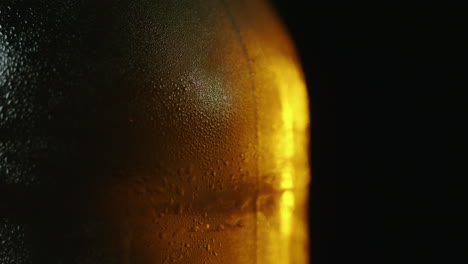 Una-Botella-De-Cerveza-Fría-Con-Gotas-De-Agua-Que-Gira-Lentamente-Se-Ilumina-Con-Un-Rayo-De-Luz-En-Un-Bl