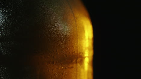 una botella de cerveza fría con gotas de agua gira lentamente y está iluminada por un rayo de luz en un bl