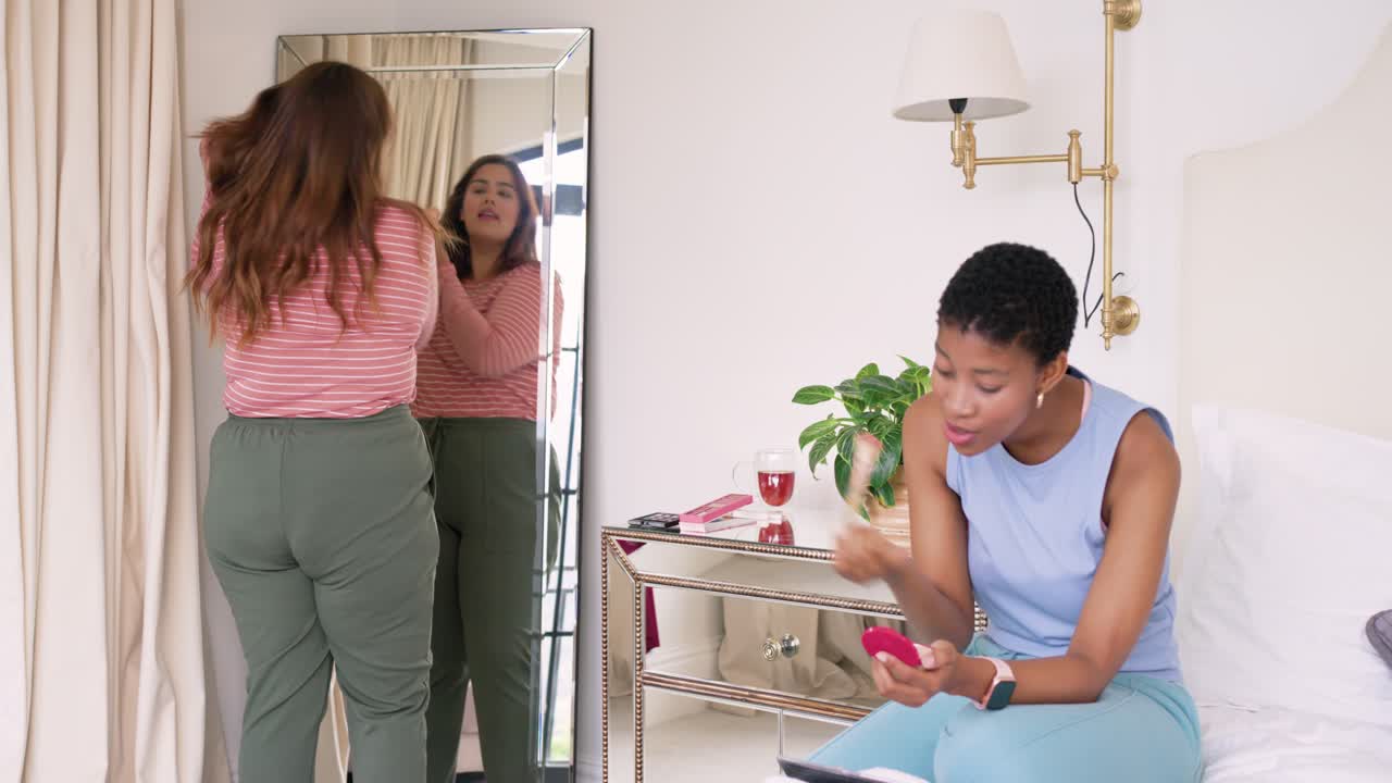 Diverse female friends wearing striped sleeveless tops prepping for party at mirror, using compact