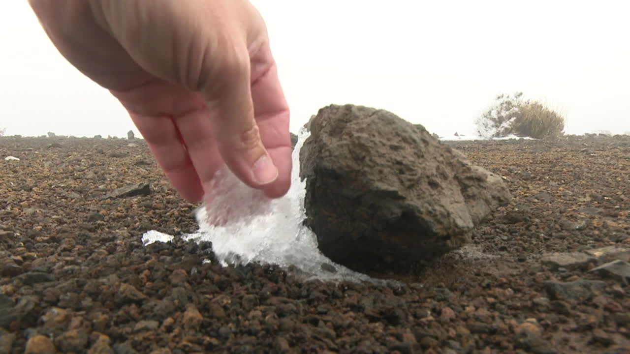 Hand touching ice-covered rock on a volcanic landscape