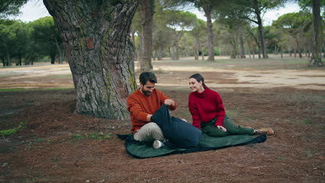 young couple sitting blanket at autumn forest vertically. tourists picnic nature