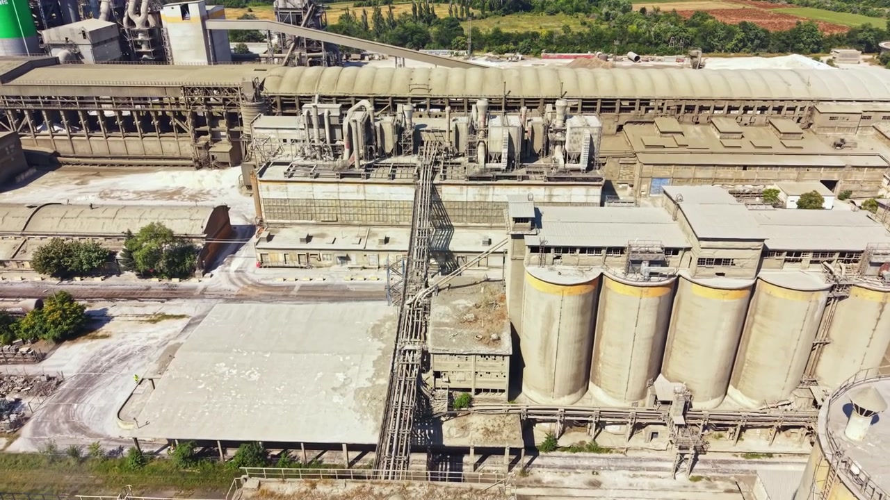 Industriestandort mit großen Silos und Fabrikgebäuden, Maschinen und Grünfläche in der Nähe.