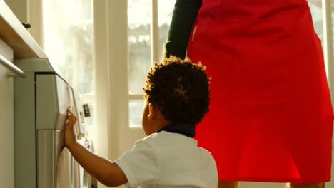 side view cute little black son playing at washing machine in kitchen of comfortable home 4k