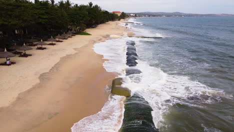 Man-made-geo-tube-protecting-sandy-beach-from-strong-ocean-waves,-aerial-fly-over-shot