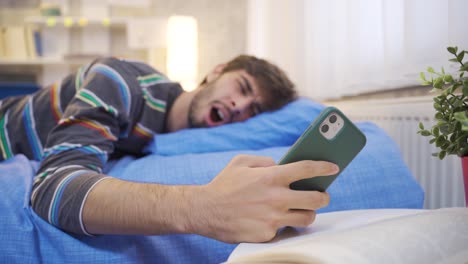 Young-man-looking-at-phone-falls-asleep-in-bed.