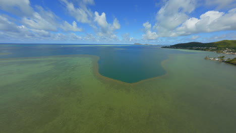 Fliegen-über-Das-Korallenriff-Atoll-Von-Hawaii,-Wolken-Voraus-Und-Berge-In-Der-Ferne,-Blaugrünes-Wasser-Und-Flauschige-Wolken