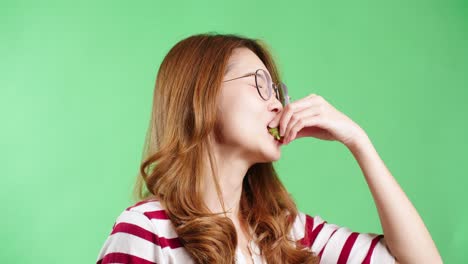 happy young asian woman in striped t-shirt wearing eyeglasses enjoy tasting and eating fresh red strawberry, green screen background