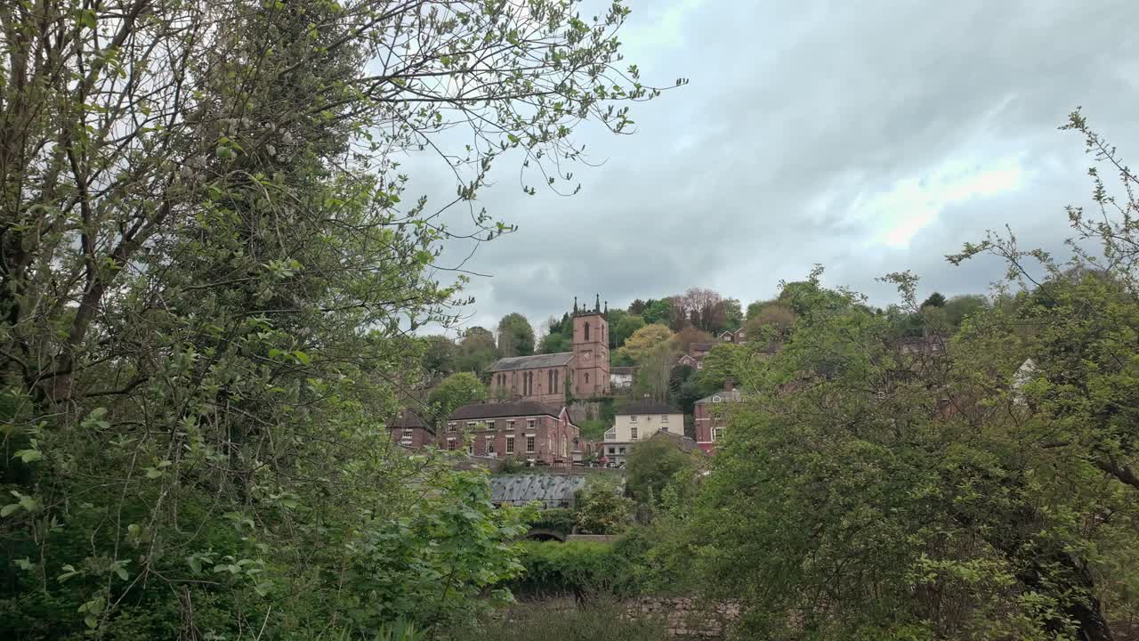 St Lukes church tower, Ironbridge seen through trees on grey day slow push shot.