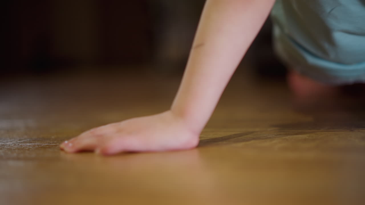 Blonde child in light blue shirt and denim shorts leans forward indoors, movement captured close-up with soft focus, showing energy, playfulness, curiosity, innocence, warm home atmosphere