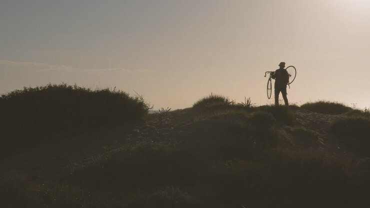 Male Carrying A Mountain Bike In The Hill Near The Beach
