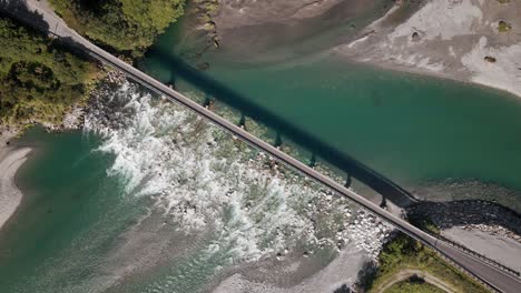 Top-down-aerial-shot-of-narrow-bridge-over-turquoise-glacier-river