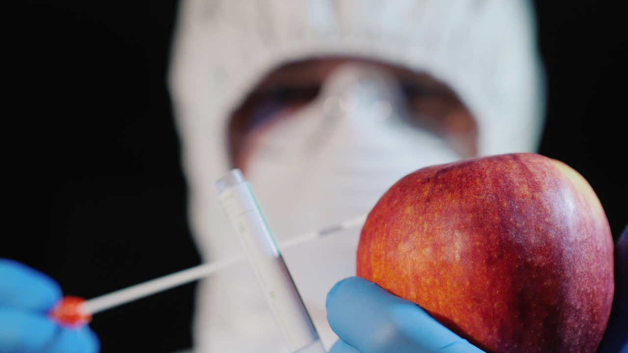 un hombre con ropa protectora y guantes toma un frotis de una manzana grande 3