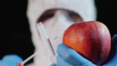 a man in protective clothing and gloves takes a smear from a large apple 3