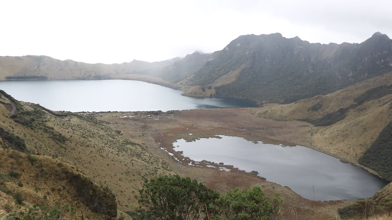 Vista panoramica a mano che si estende verso sinistra attraverso i laghi vulcanici di Mojanda e le imponenti vette andine in Ecuador, ideale per produzioni di viaggio, natura e documentari.