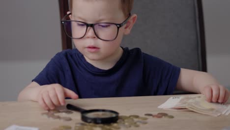 caucasian baby in glasses playing with euro money coins banknotes and magnifier