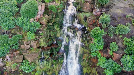 Stunning-Yorkshire-Moors-waterfall,-aerial-view-shows-water-cascading-over-rocks-into-a-deep-pool,-hikers-below